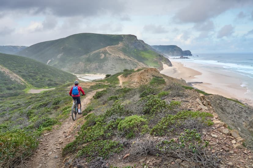 happy active senior woman cycling on the the rocky cliffs of the Vicentina coast of Algarve, Portugal near Sagres and Vila do Bispo
